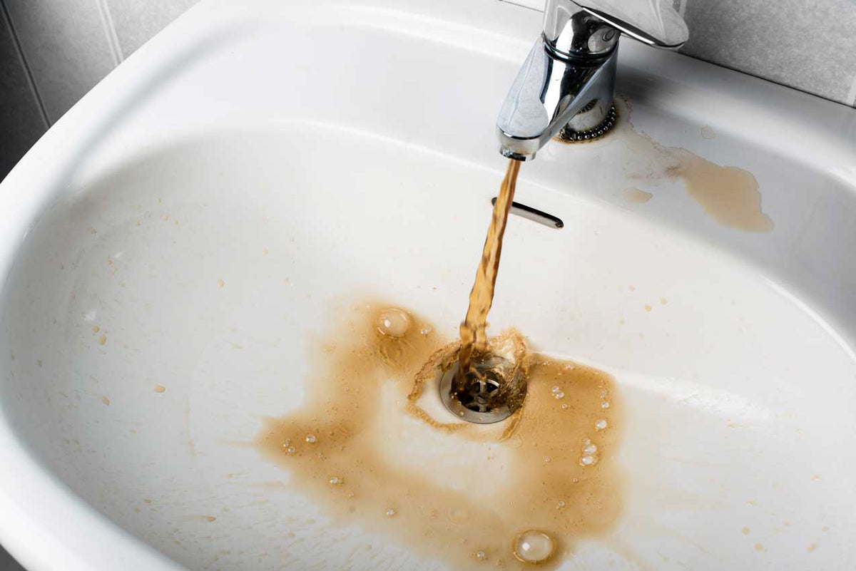 Braunes, rostiges Wasser läuft aus dem Wasserhahn in ein fleckiges weißes Waschbecken