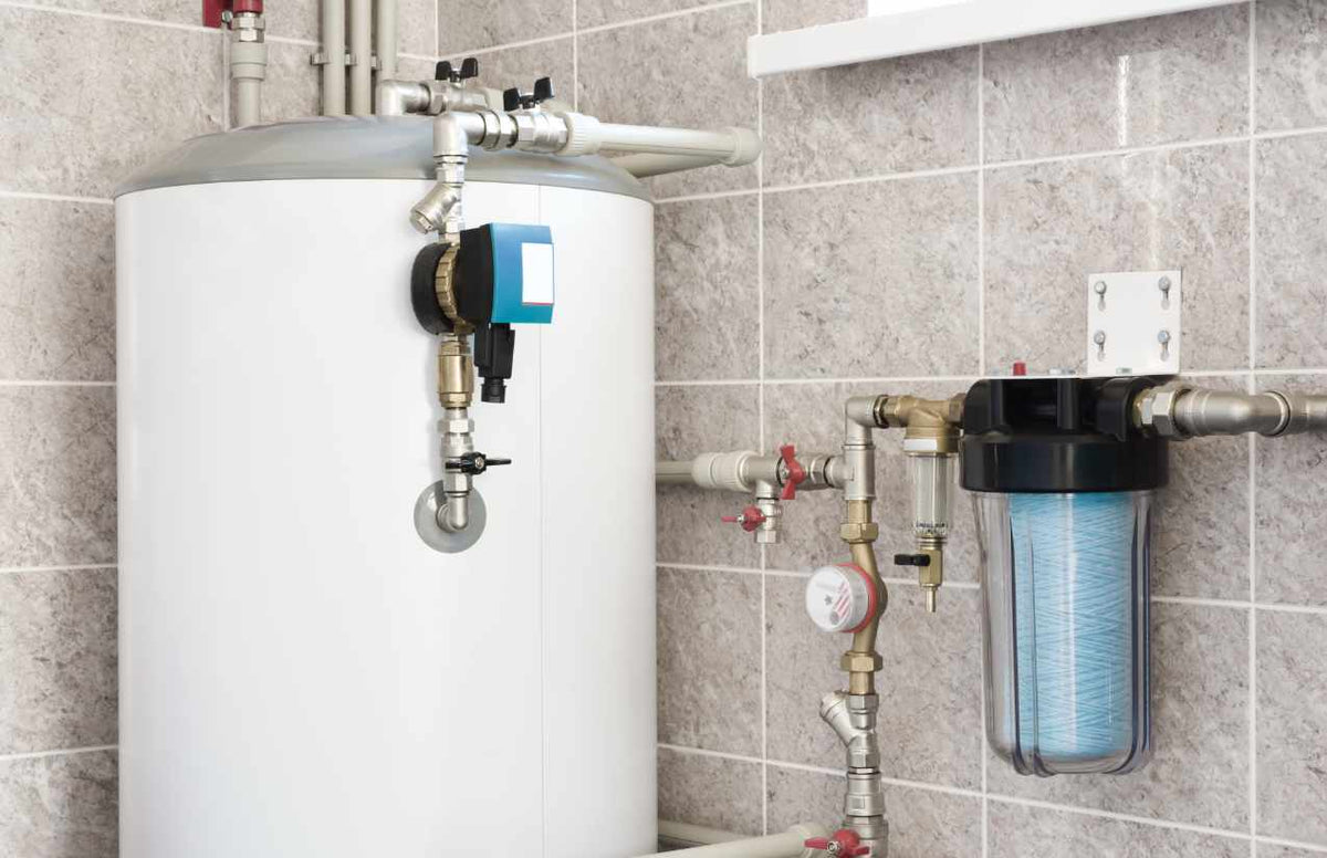 Hauswasserfilter mit klarem Filtertopf neben Warmwasserspeicher im gefliesten Technikraum