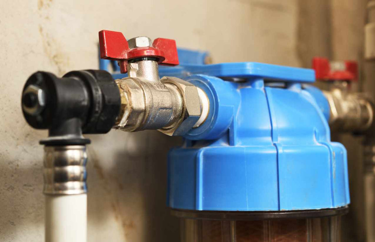 Blauer Hauswasserfilter mit rotem Absperrhahn und Verschraubung an einer Kellerwand