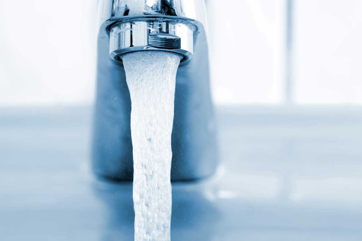 Verchromter Wasserhahn mit kräftigem Wasserstrahl über einem Becken, blau getönte Nahaufnahme