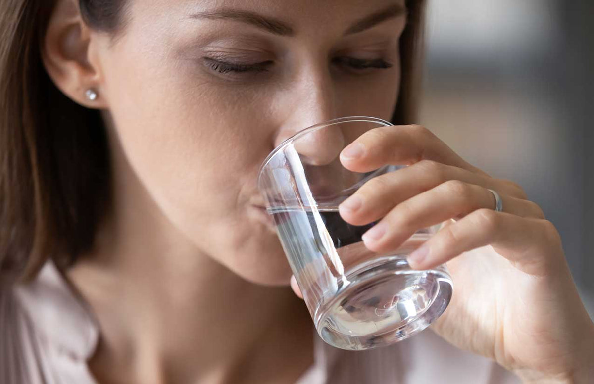 Nahaufnahme einer Frau, die zögerlich aus einem Glas Leitungswasser trinkt