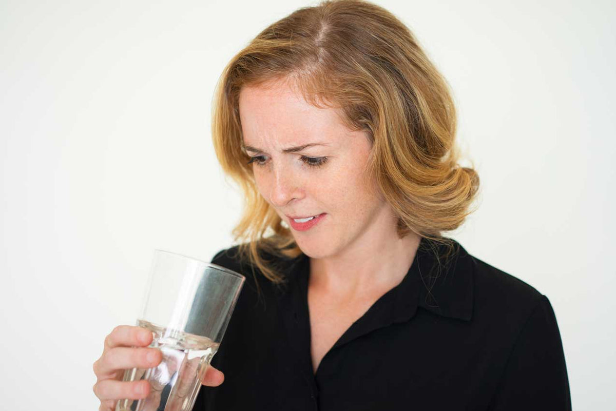 Frau mit angewidertem Gesichtsausdruck riecht an einem Glas Leitungswasser