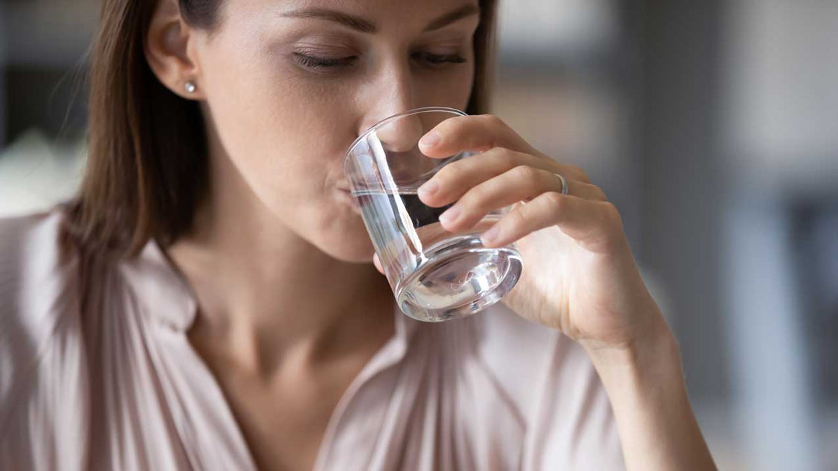 Junge Frau nippt mit geschlossenen Augen zögerlich an einem Glas Leitungswasser