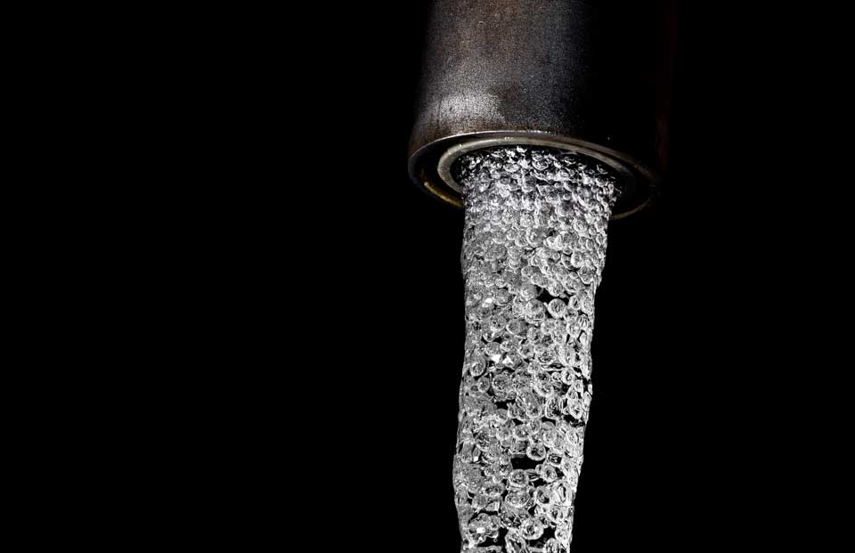 Dunkler Wasserhahn vor schwarzem Hintergrund mit stark sprudelndem, trübem Wasserstrahl