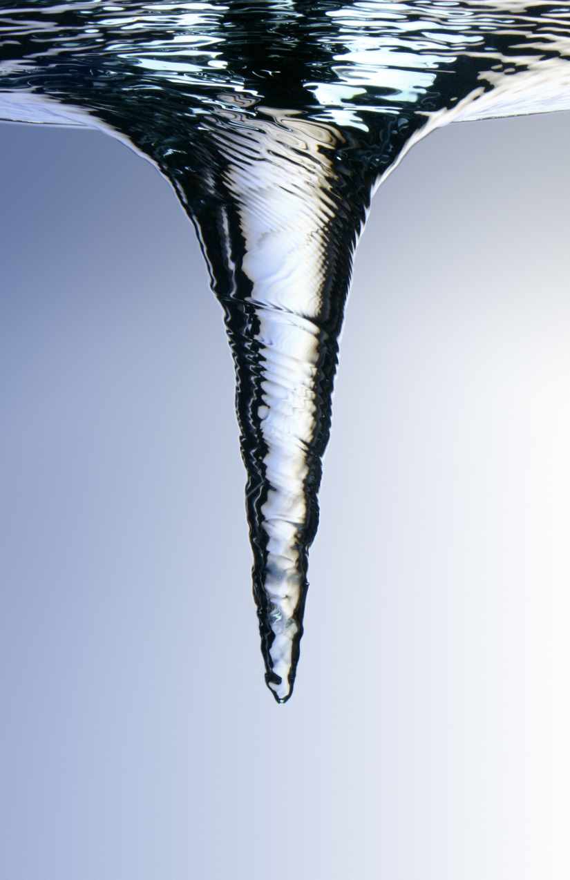 Trichterförmiger Wasserwirbel mit fein geriffelter Oberfläche vor blau-weißem Hintergrund