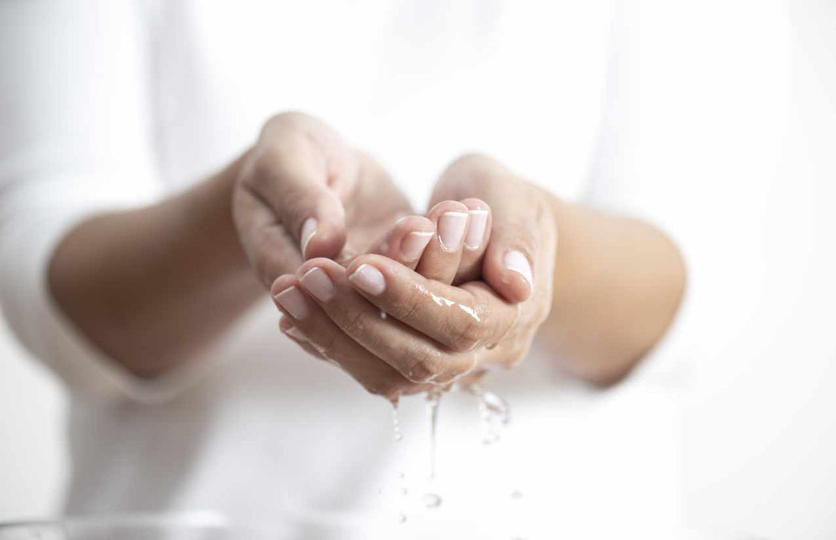 Zu einer Schale geformte Hände, aus denen klares Wasser tropft, vor weißer Kleidung