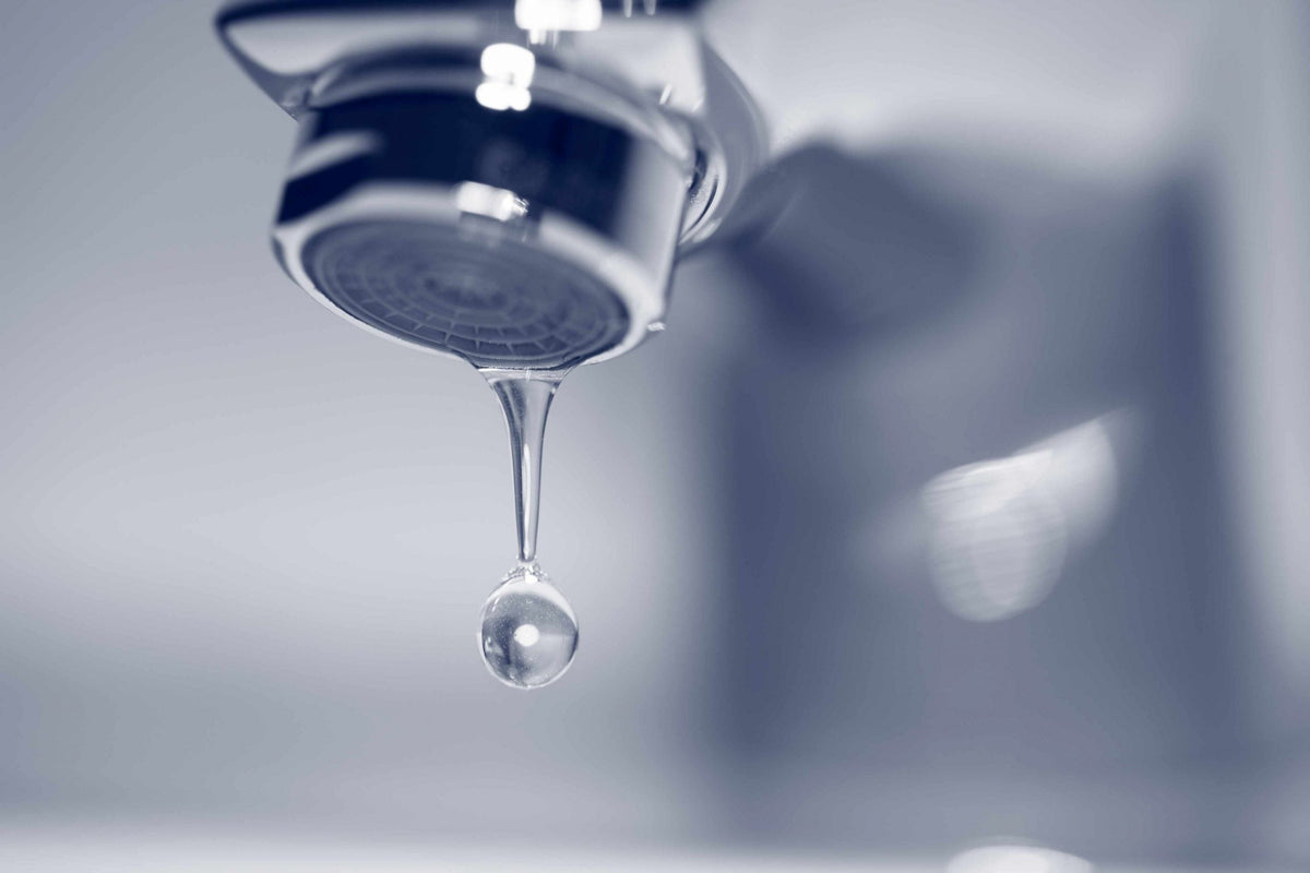 Einzelner Wassertropfen löst sich vom Perlator eines Wasserhahns, Nahaufnahme in Blaugrau
