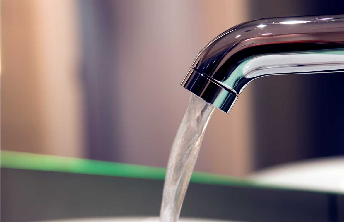 Verchromter Wasserhahn mit dünnem laufenden Wasserstrahl über einem Waschbecken