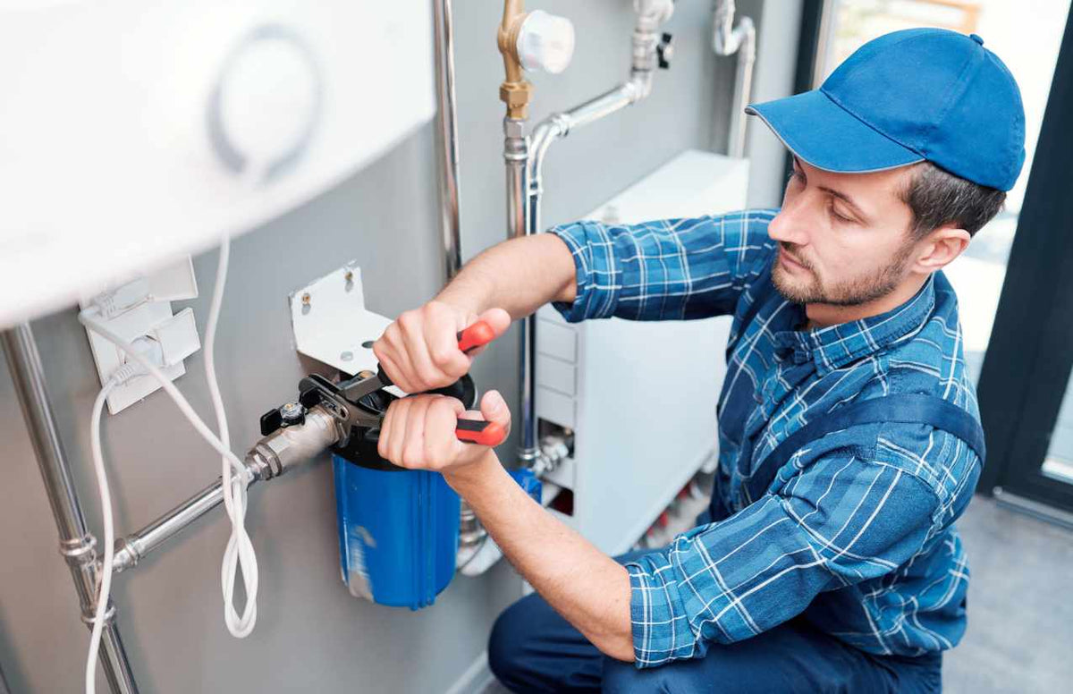 Installateur mit blauer Kappe montiert ein blaues Filtergehäuse an der Hausinstallation