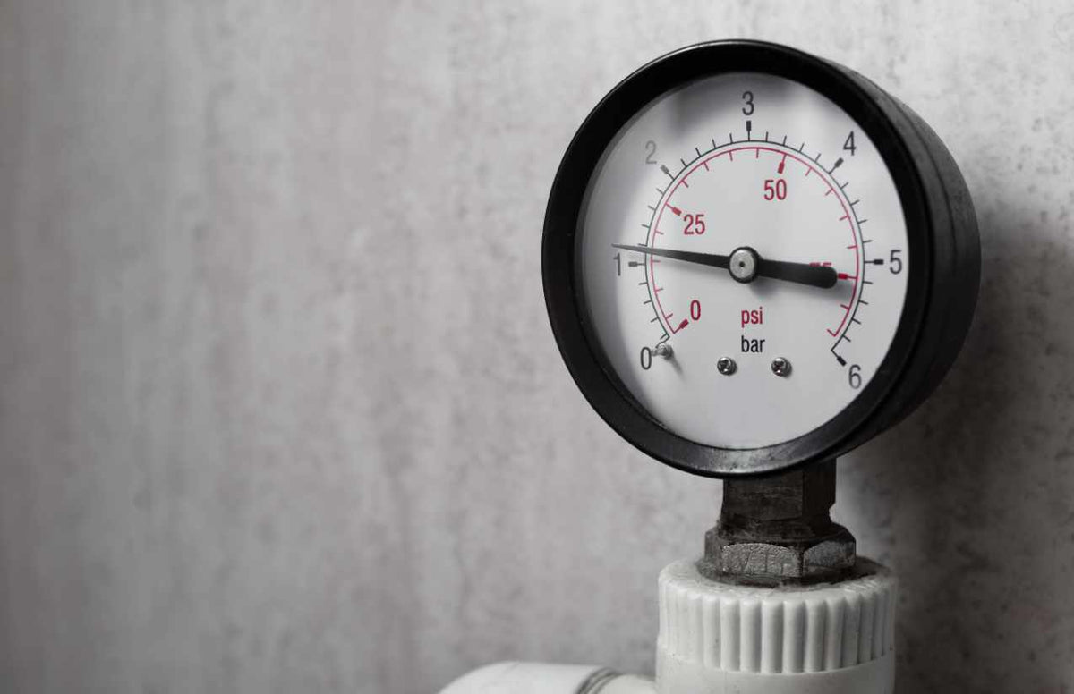 Manometer mit bar- und psi-Skala an einer Wasserleitung vor grauer Betonwand