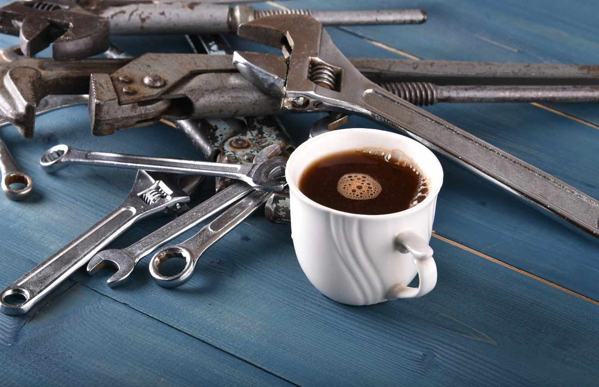 Rohrzangen und Schraubenschlüssel neben einer Tasse Kaffee auf blauem Holztisch