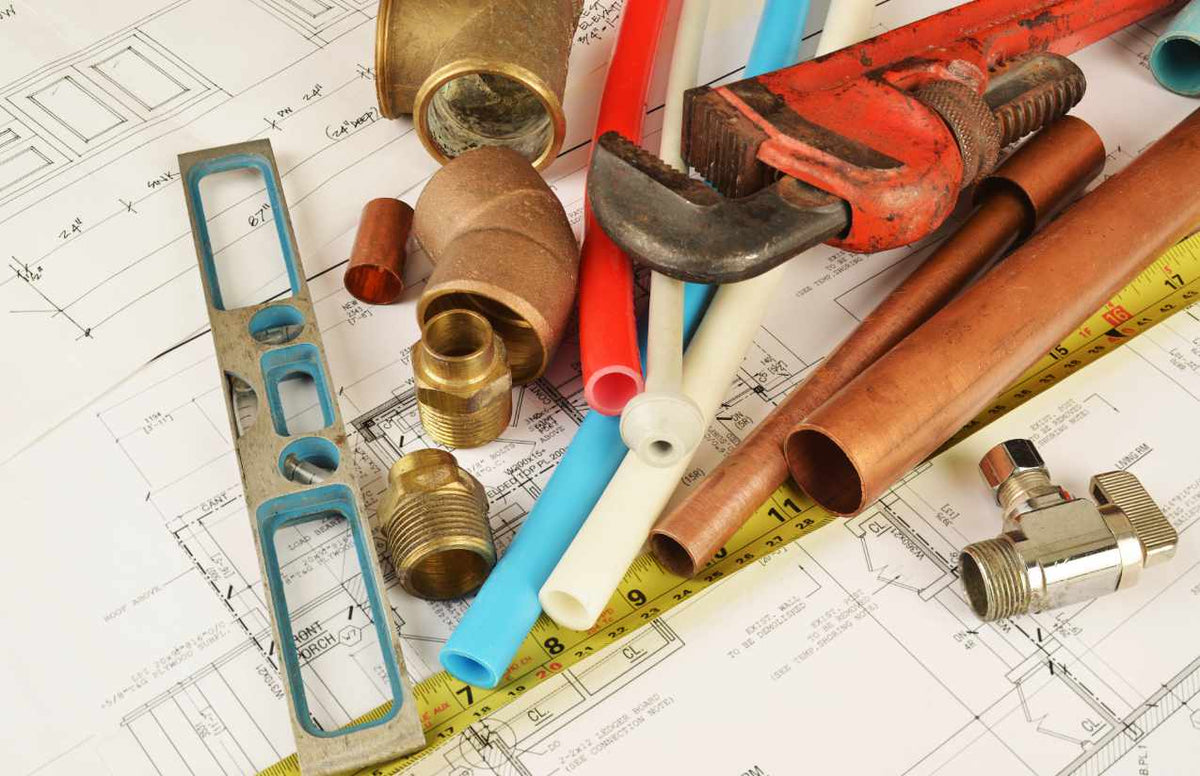Kupferrohre, Kunststoffleitungen und Messingfittings mit Rohrzange und Wasserwaage auf einem Bauplan