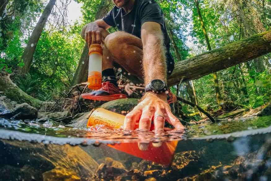 Mann entnimmt Wasser aus Bach mit Geopress-Flasche