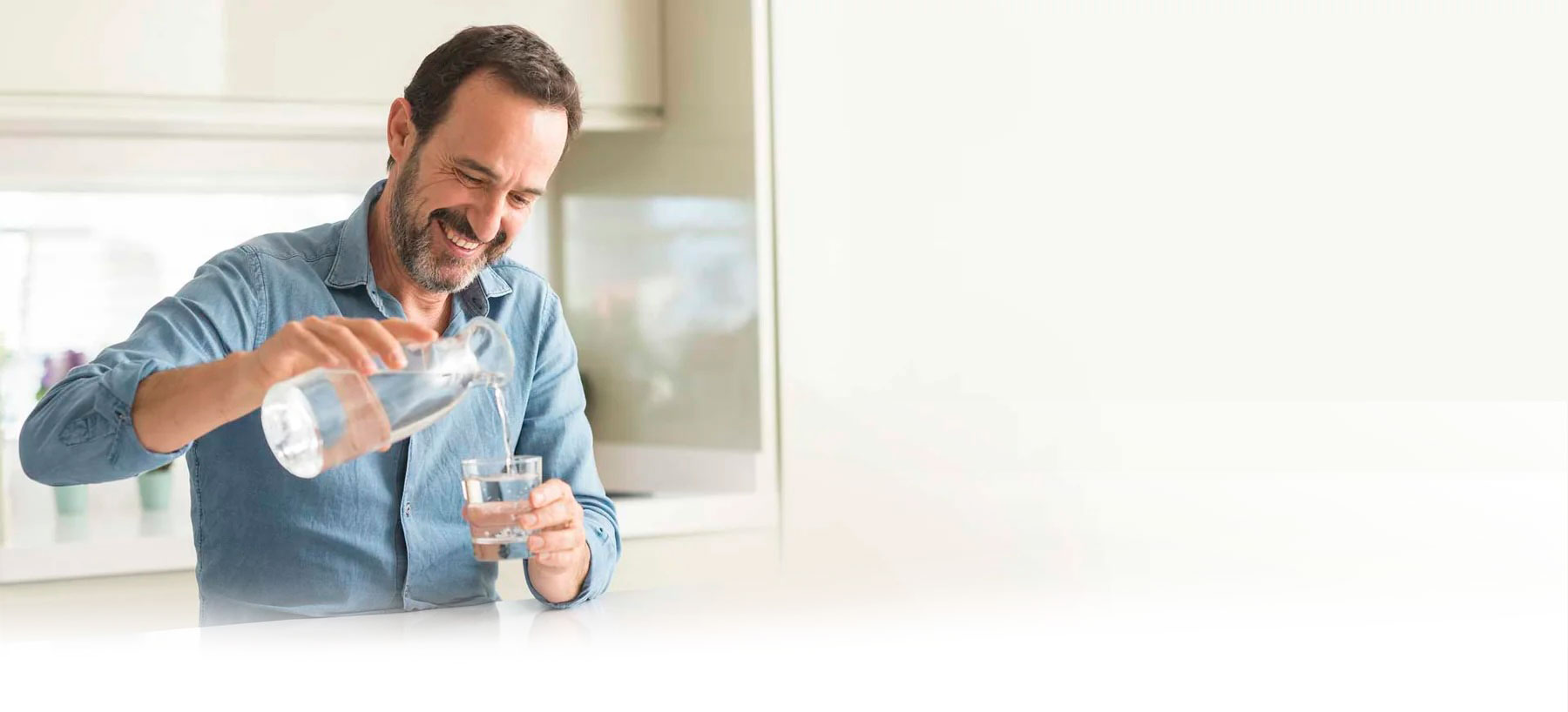 glücklicher Mann gießt sich gefiltertes Wasser ins Glas