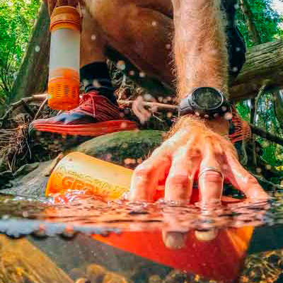 Mann befüllt Outdoor Wasserfilter mit Wasser aus einem Bach