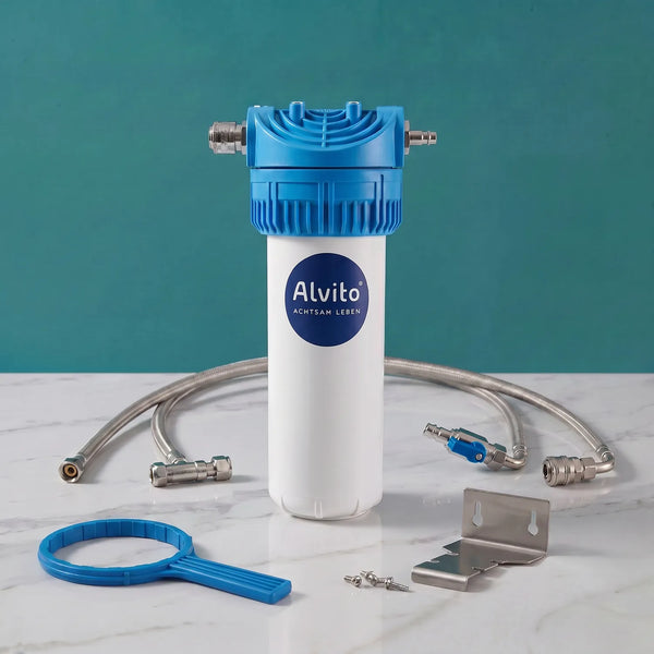 Alvito Basic Einbaufilter-Set auf weißer Marmorarbeitsplatte – blau-weißes Filtergehäuse mit Alvito-Logo, zwei Flexschläuche, blauer Filterschlüssel (Ringform), Edelstahl-Wandhalterung, Schrauben und blaues Kugelventil; teal Hintergrund