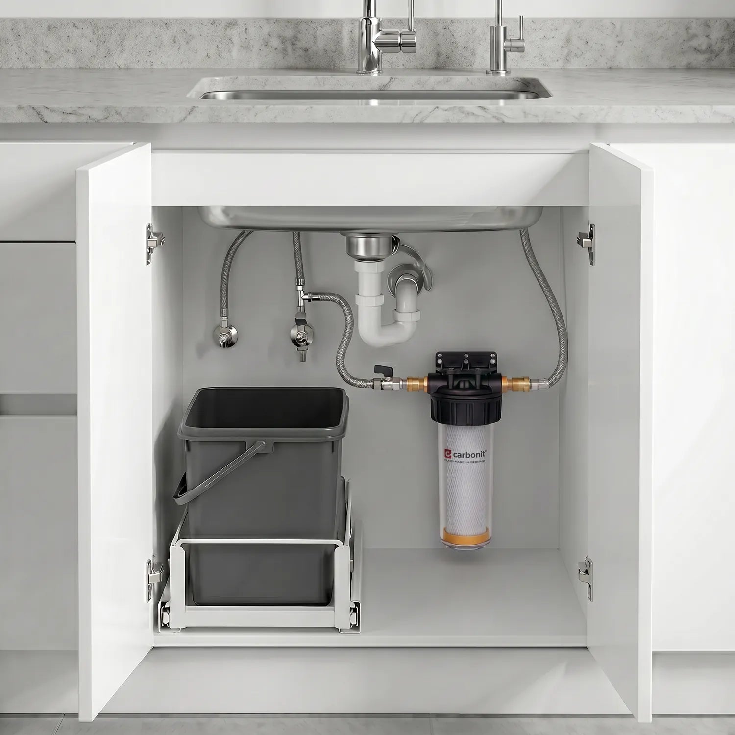 Carbonit Vario-HP Comfort im offenen Unterschrank – transparentes Gehäuse mit IFP-Puro-Kartusche (orange Bodenkappe) und schwarzem Kopf, rechts an weißer Schrankwand montiert; grauer Müllcontainer auf Ausziehschienen links; Edelstahlspüle, P-Trap, Absperrventile und Zuleitungen oben; Marmor-Arbeitsplatte und 1-Wege-Hahn, helle moderne Küche