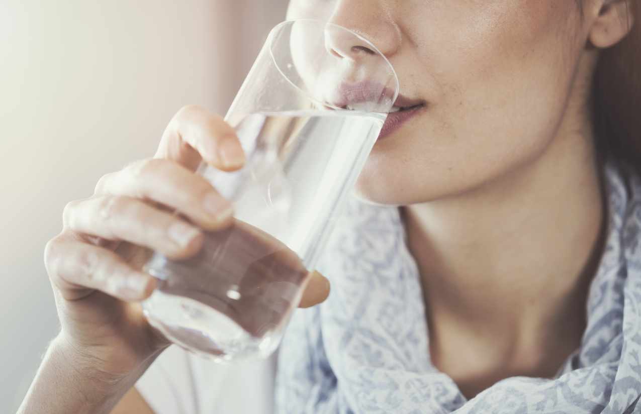 Junge Frau trinkt klares Wasser aus einem Glas, Nahaufnahme von Hand und Mund