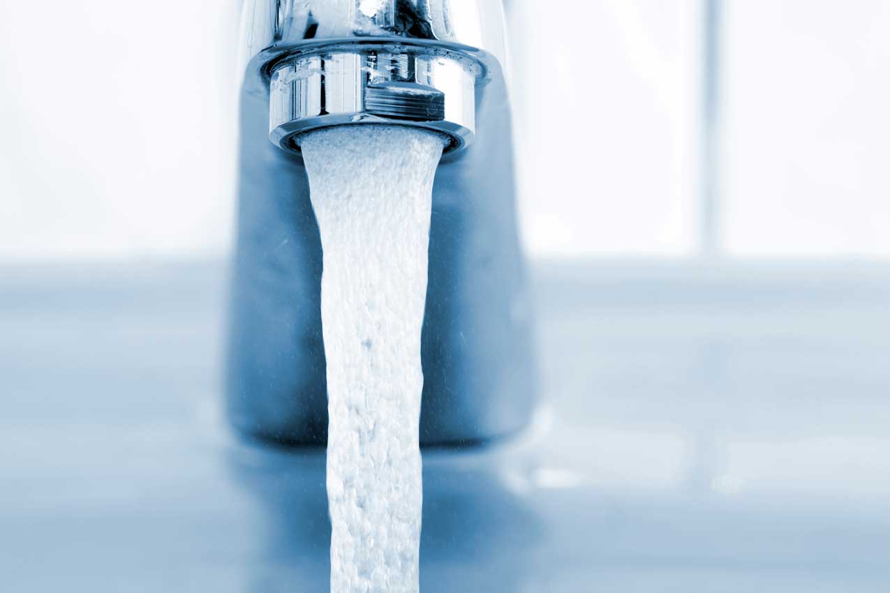Verchromter Wasserhahn mit kräftigem Wasserstrahl über einem Becken, blau getönte Nahaufnahme