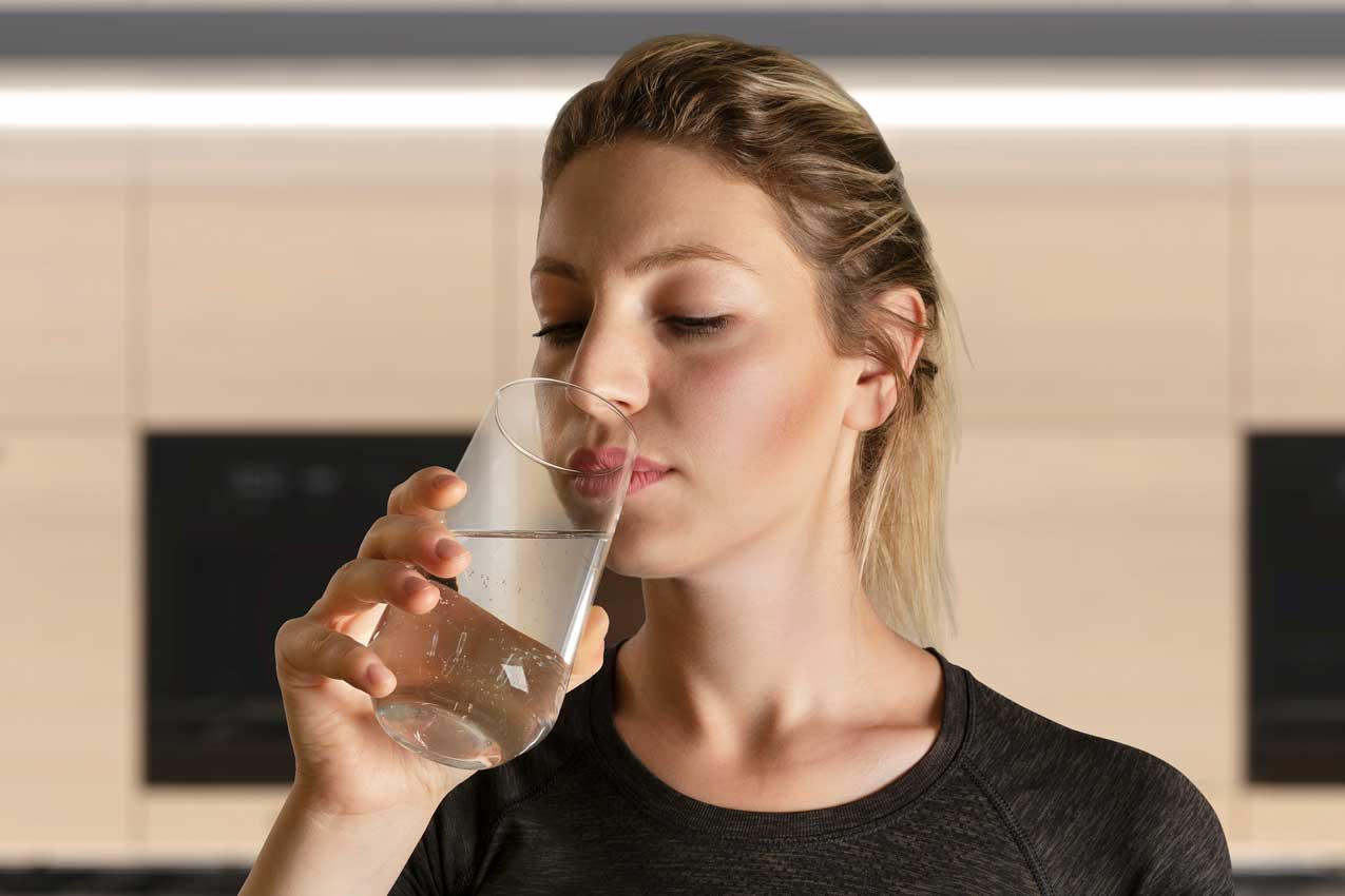 Junge Frau in der Küche setzt ein Glas Wasser an und prüft dessen Geruch