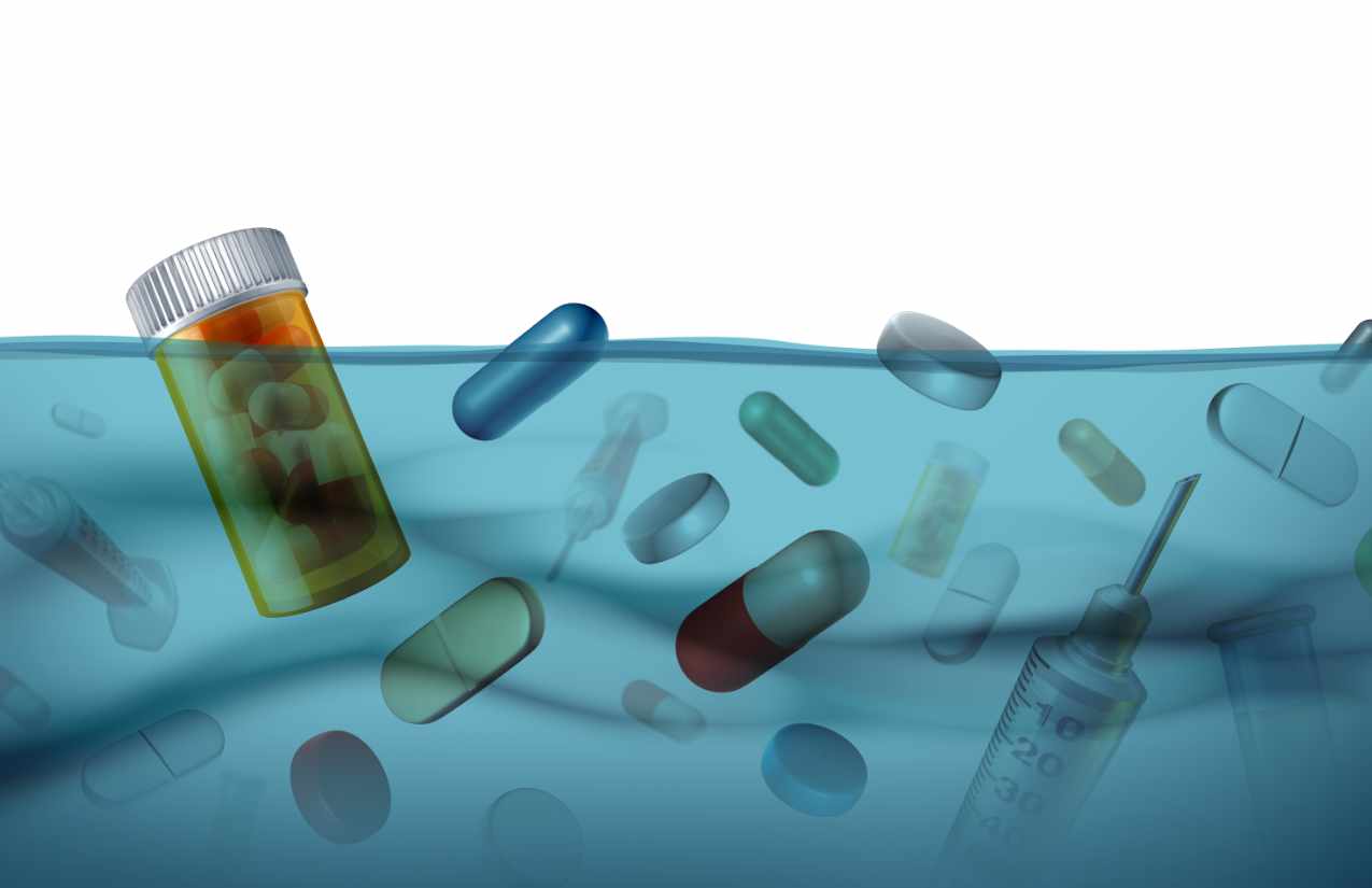 Tabletten, Kapseln, eine Tablettendose und eine Spritze treiben halb untergetaucht in blauem Wasser