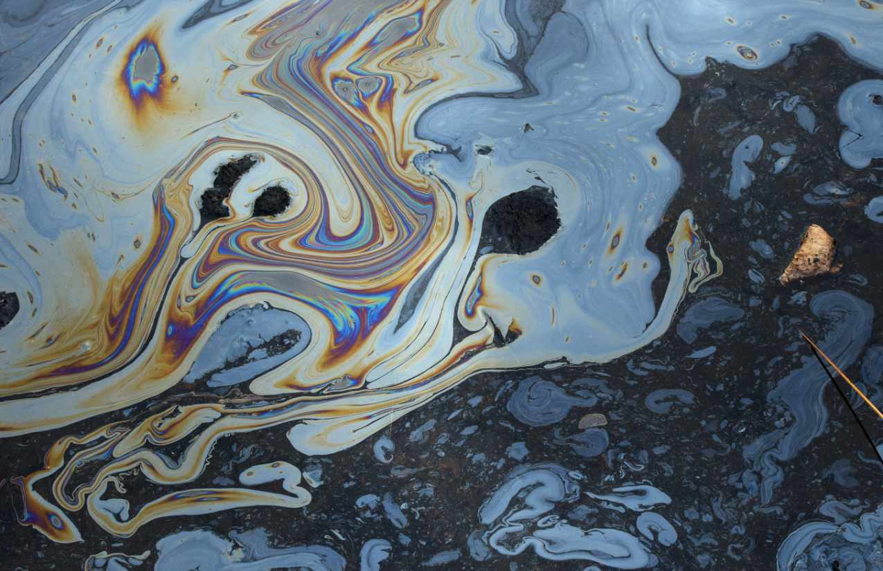 Schillernder Ölfilm auf dunkler Wasseroberfläche mit regenbogenfarbenen Schlieren