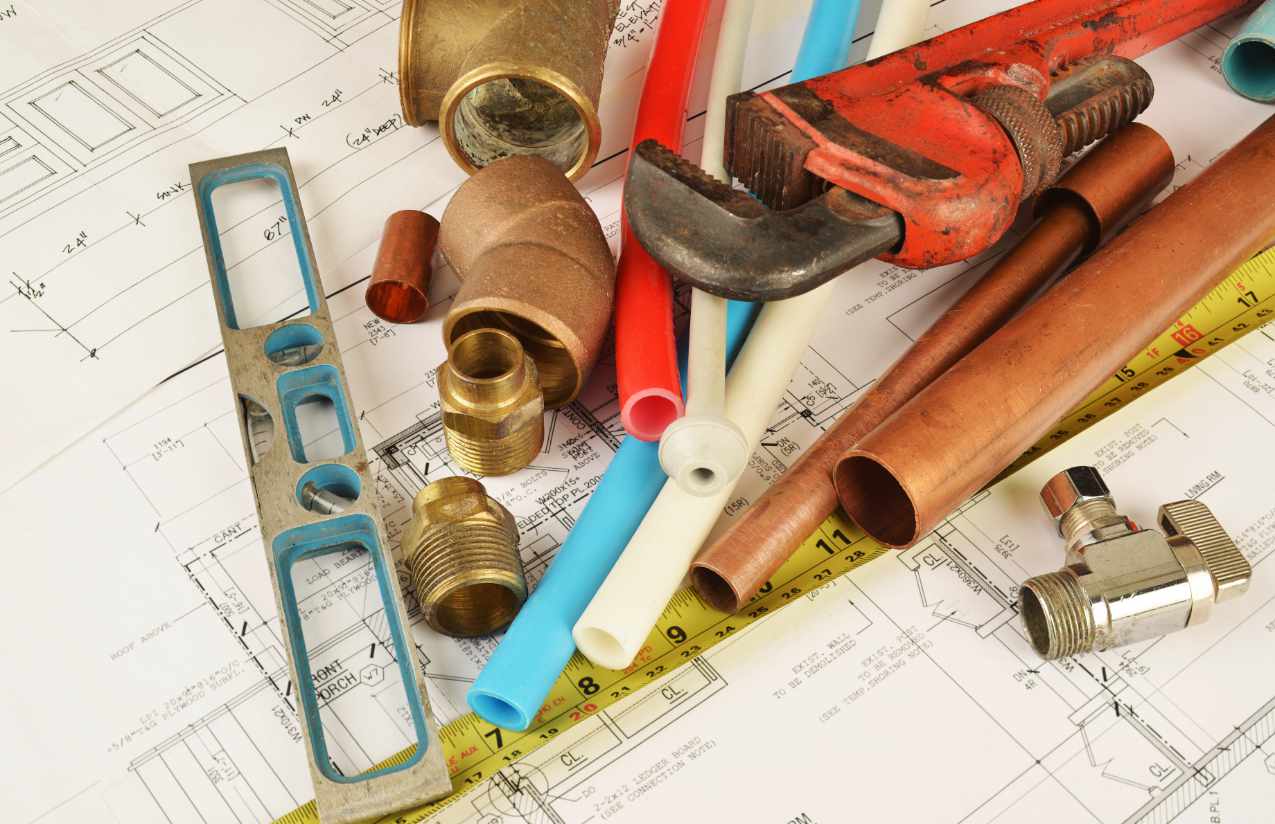 Kupferrohre, Kunststoffleitungen und Messingfittings mit Rohrzange und Wasserwaage auf einem Bauplan