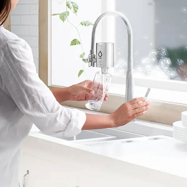 Frau gießt sich gefiltertes Wasser aus Wasserhahnfilter