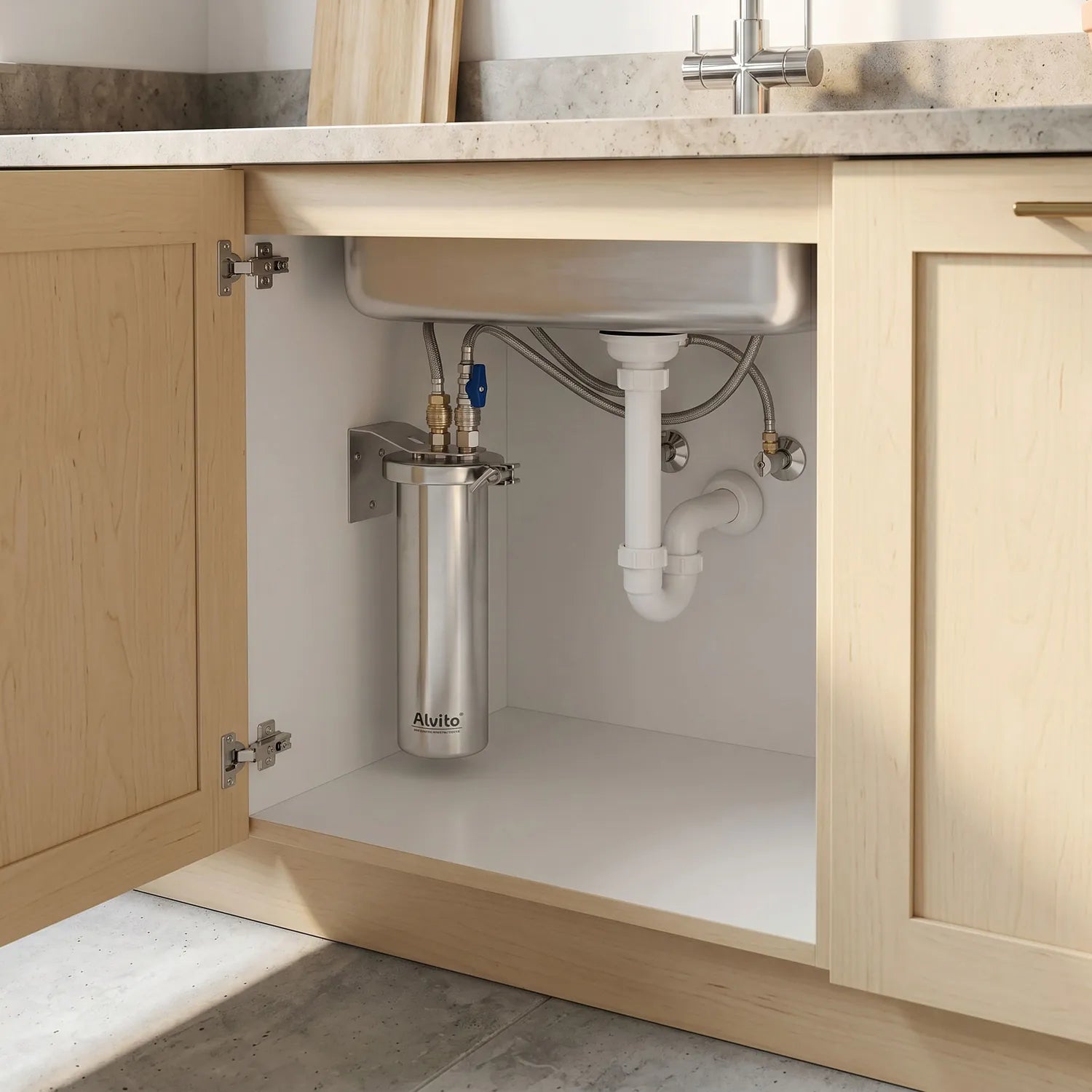 Alvito Inox T Einbaufilter montiert im offenen Unterschrank – gebürstetes Edelstahlgehäuse mit Schmetterlingsklemme an hellem Holzschrank-Innenwand; Schlauchverbindungen und blaues Kugelventil sichtbar; Marmorarbeitsplatte und Chrom-Hahn oben im Bild