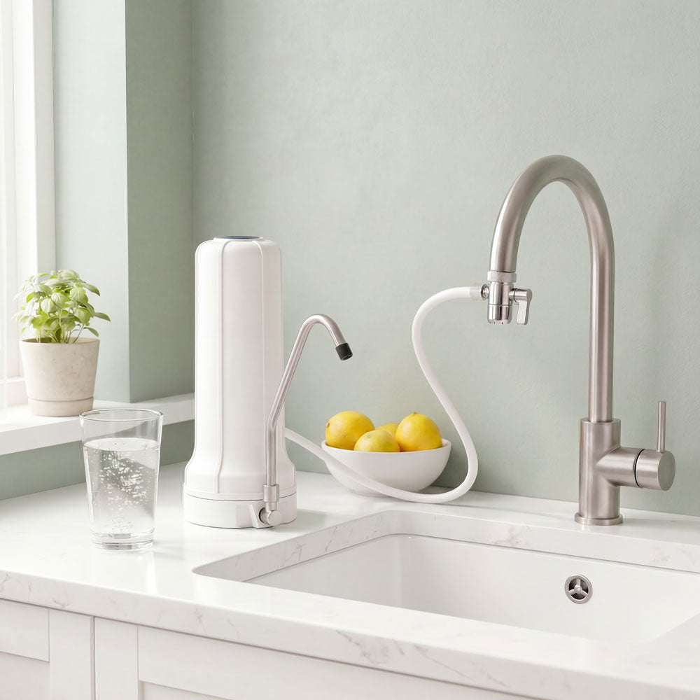 Weißer Auftischfilter auf Marmorarbeitsplatte mit eigenem Chromhahn, Glas Wasser und Zitronen in minimalistischer Küche