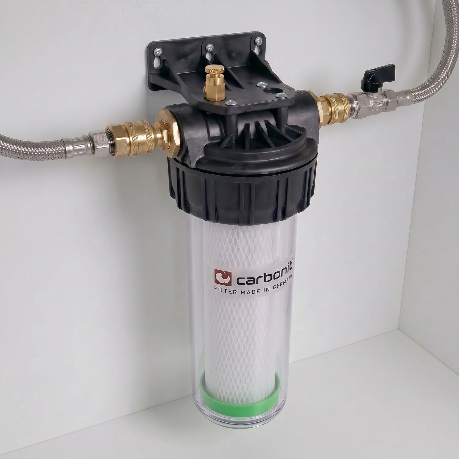 Carbonit Vario-HP Küche montiert an weißer Schrankwand – transparentes Gehäuse mit weißer NFP-Filterkartusche (Kreuzstruktur, grüner Ring), schwarzer Kopf mit Messing-Schnellkupplungen und Entlüftungsschraube