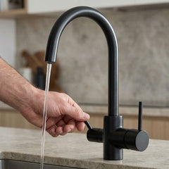 Hand bedient schwarzen 3-Wege-Hahn mit fließendem Wasser auf heller Steinarbeitsplatte in moderner Küche